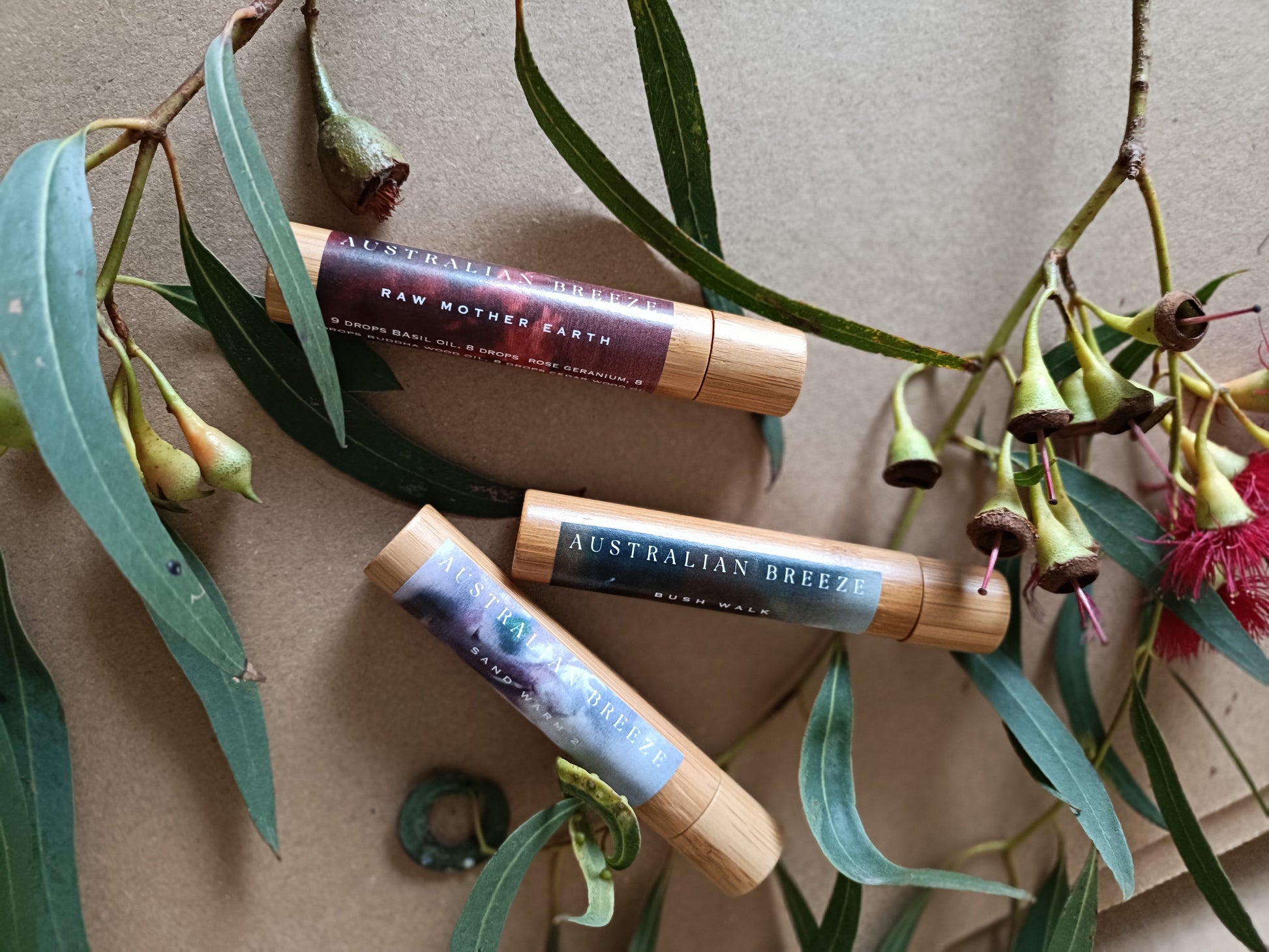 Three Roll-on-perfume tubes with 'Australian  label on a textured surface with green leaves and flowers.