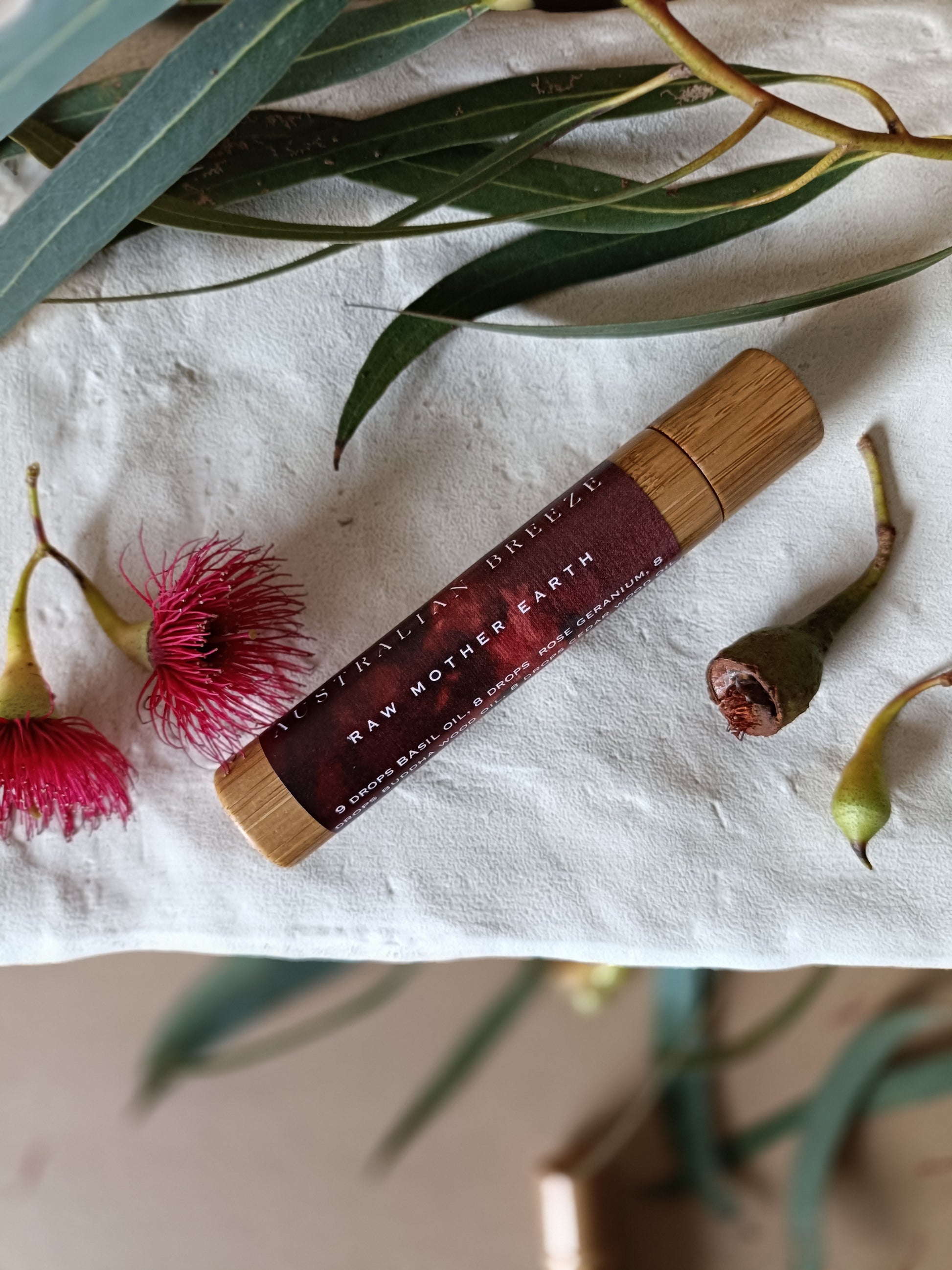 Roll-on-perfume with wooden cap on a white stone with green leaves and pink flowers