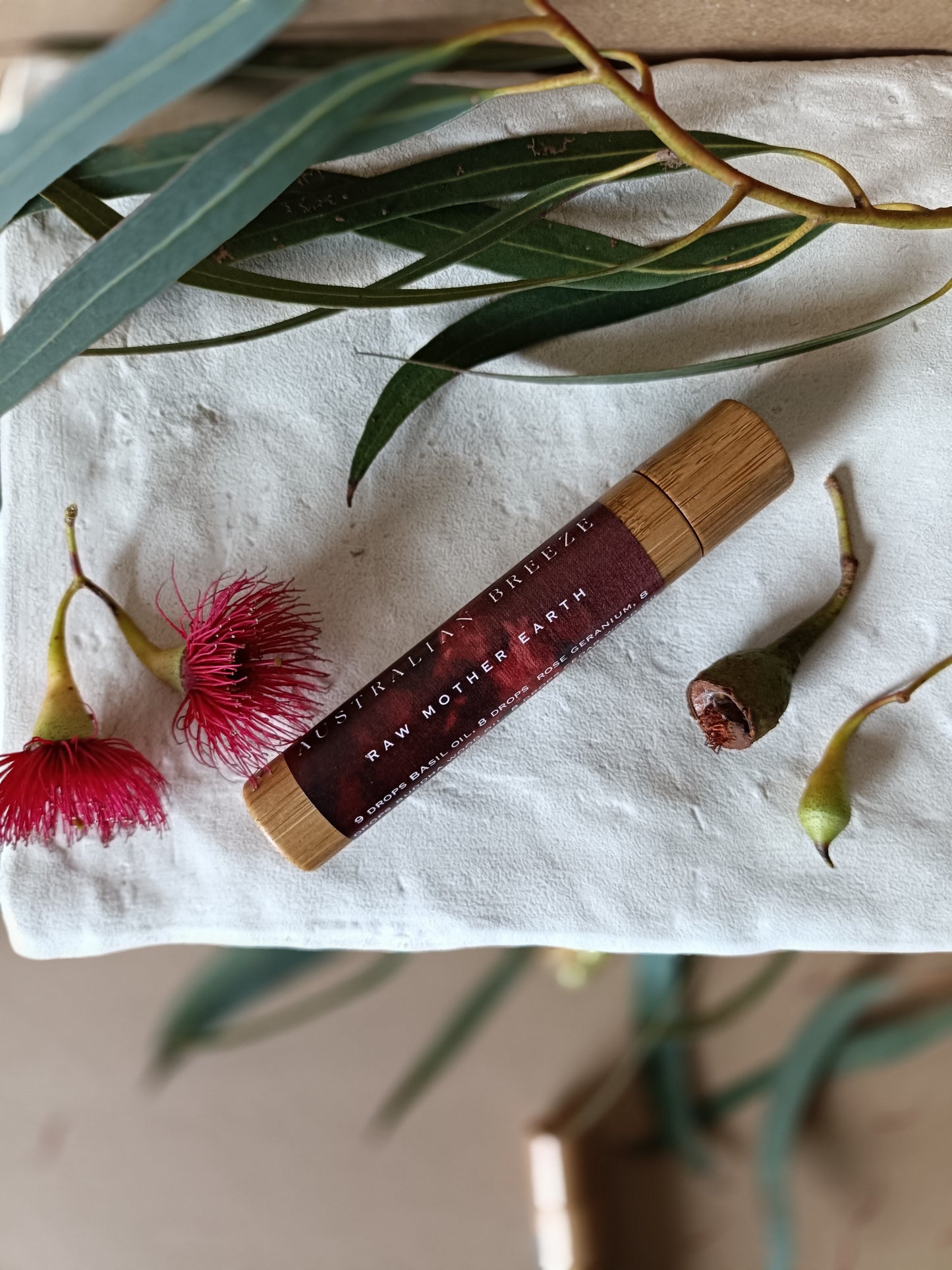 Cosmetic tube with a wooden cap on a white stone with green leaves and  eucalyptus pink flowers.