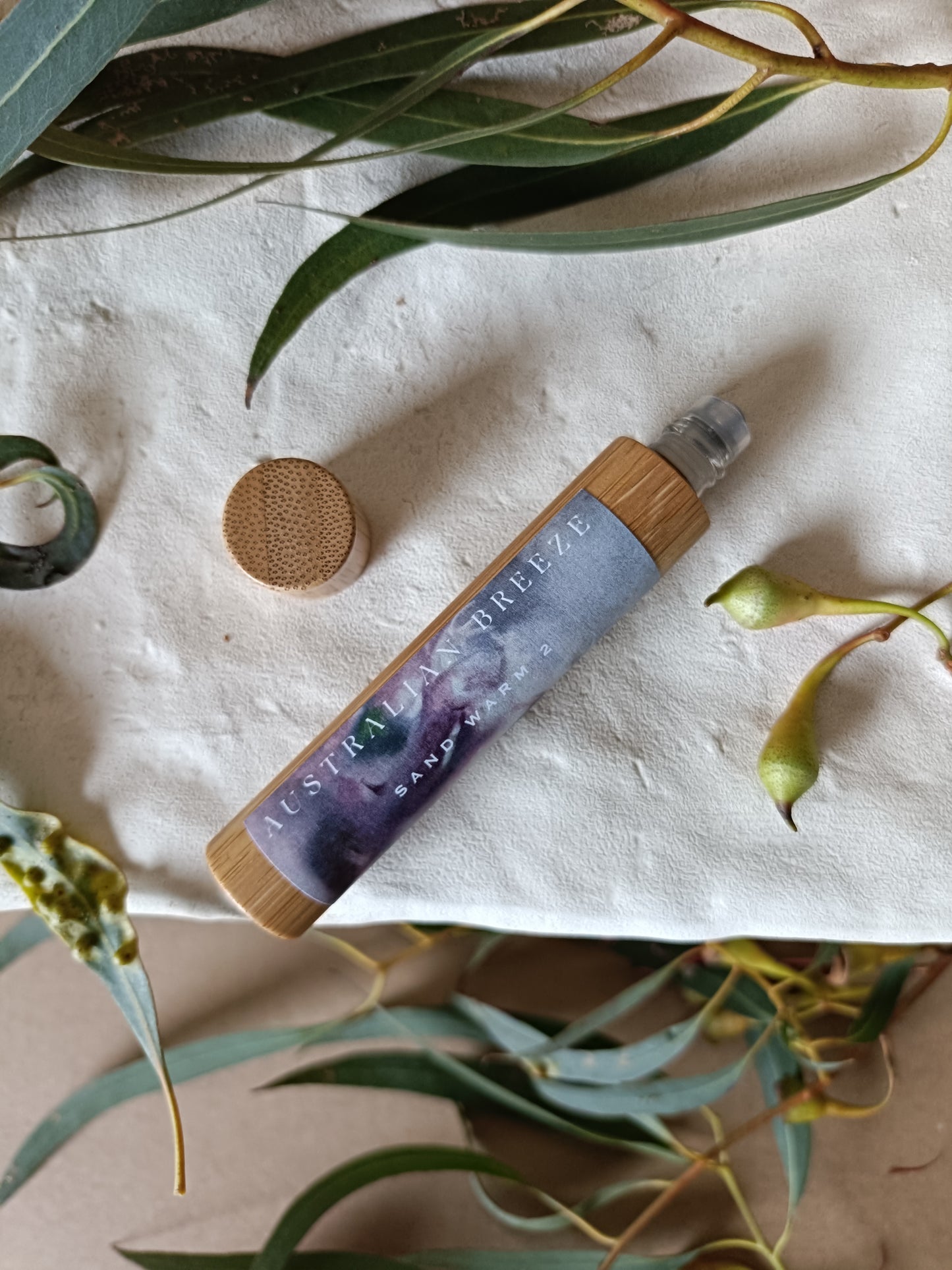 Perfume bottle with wooden cap and label on a textured surface with green leaves
