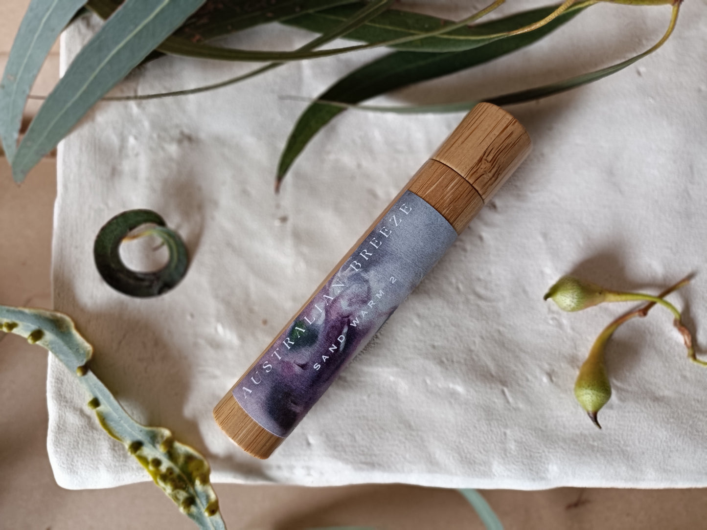 Roll-on-perfume product with wooden cap on a textured surface with green leaves