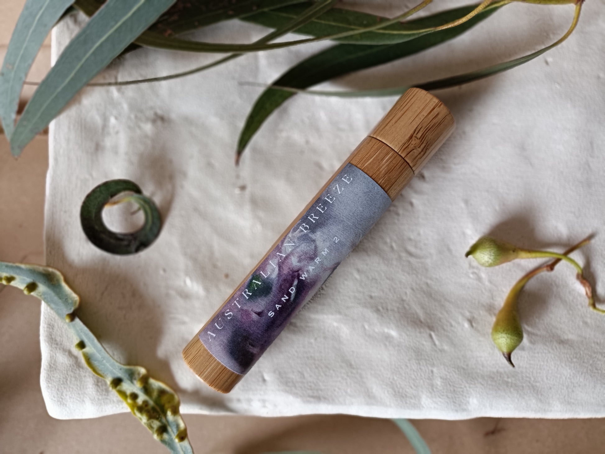 Roll-on-perfume product with wooden cap on a textured surface with green leaves